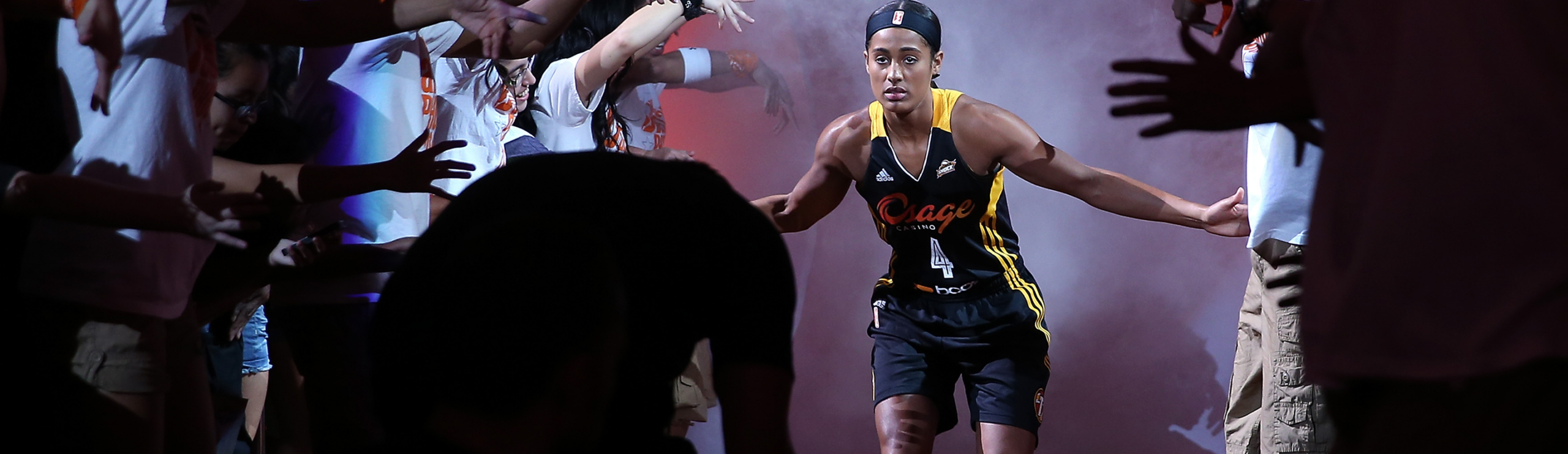 WNBA player runs onto the court through a smoke-filled tunnel, high-fiving fans reaching out from both sides
